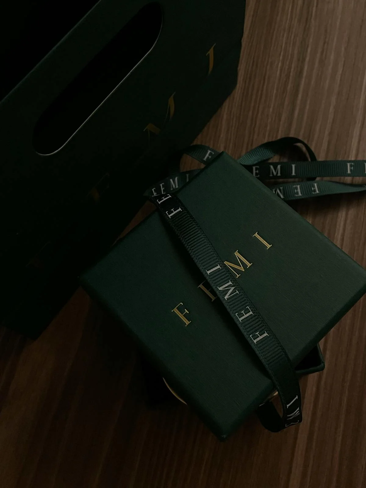 Deep green jewelry box with gold foil stamped logo and branded ribbon bow